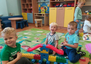 Trzech chłopców siedzi na dywanie i buduje pociąg z klocków